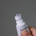 Imagem em grande plano da mão de uma pessoa a segurar o Cica Farm Revitalizing Rolling Eye Serum com três esferas metálicas na ponta. O gel transparente é visível. O fundo é cinzento liso.