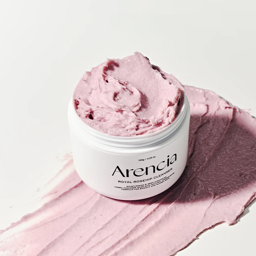 Um frasco rosa rotulado "Arencia Fresh Rosehip Rice Mochi Cleanser", com um creme rosa macio e fofo por cima. Transmite uma sensação hidratante e calmante.