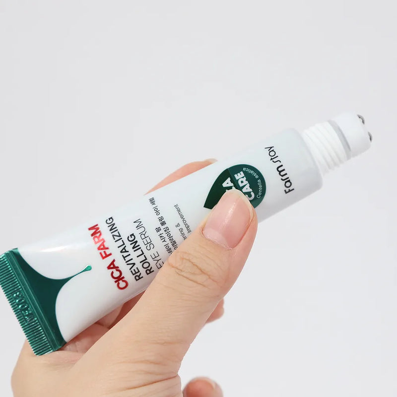 Imagem em grande plano da mão de uma pessoa a segurar o Cica Farm Revitalizing Rolling Eye Serum com três esferas metálicas na ponta. O gel transparente é visível. O fundo é cinzento liso.