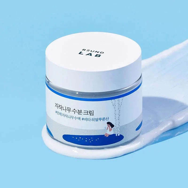 Creme hidratante coreano em pote branco com ilustração de bétula e menina, rotulagem em coreano.