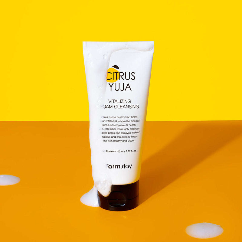 Tubo branco do Citrus Yuja Vitalizing Foam Cleansing sobre uma superfície laranja, com espuma a transbordar, sobre um fundo amarelo brilhante. Tom fresco e vibrante.