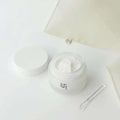 Creme facial hidratante coreano branco em pote aberto sobre superfície clara, com espátula.