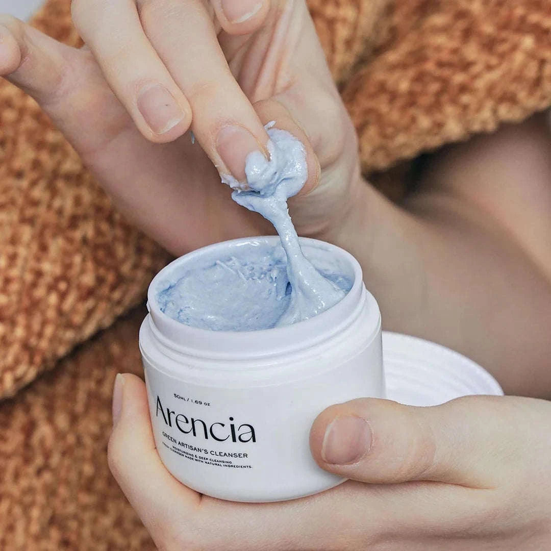 Um frasco do Arencia Fresh Blue Hyssop Rice Mochi Cleanser, aberto para revelar o creme azul-claro e a sua textura. 