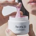 Uma mão estica um creme de limpeza rosa de um frasco branco rotulado 