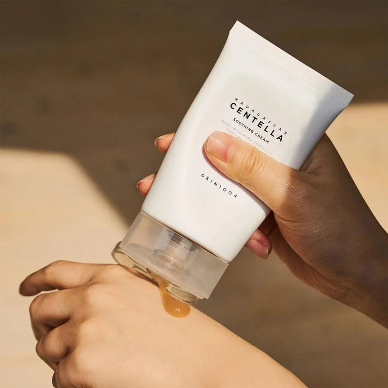 Mãos aplicando creme calmante Centella SKIN1004 na pele, cuidado facial coreano.