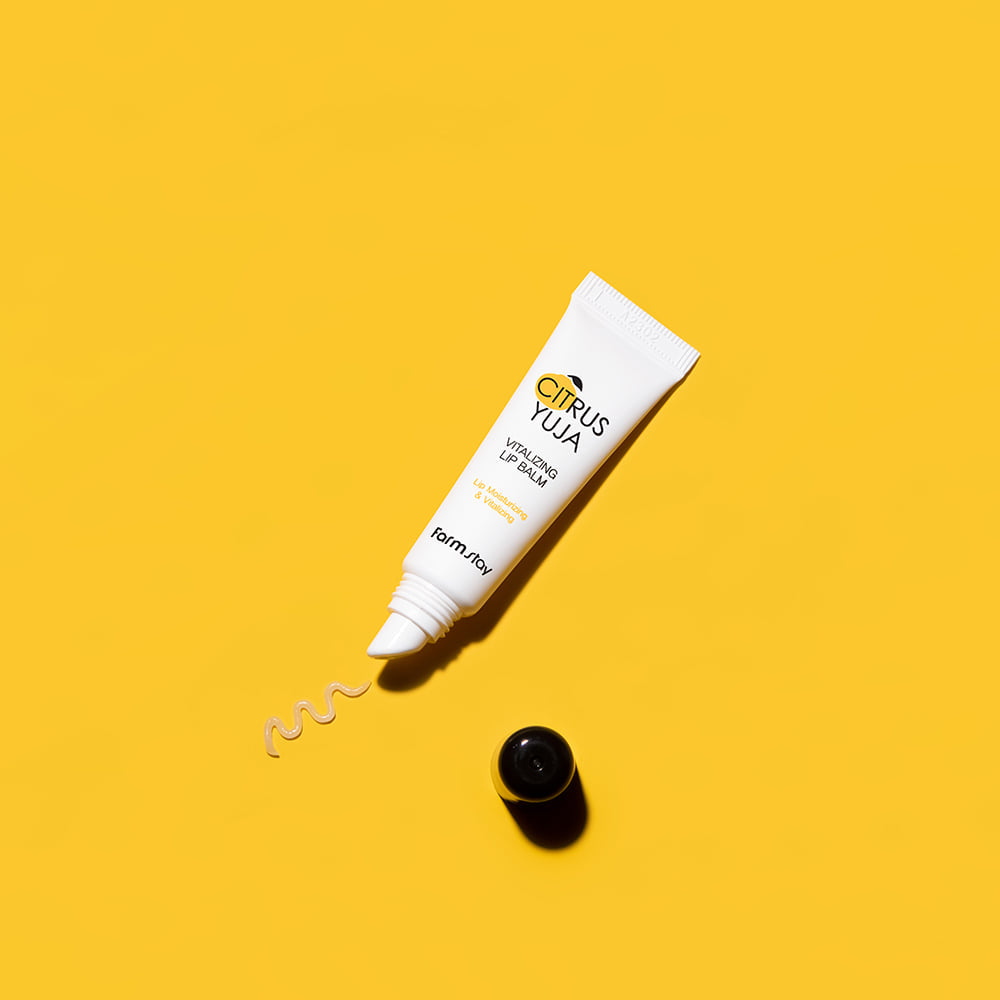 Tubo do Citrus Yuja Vitalizing Lip Balm sobre um fundo amarelo vibrante, com uma pequena mancha do bálsamo visível. A imagem transmite uma sensação de energia e frescura.