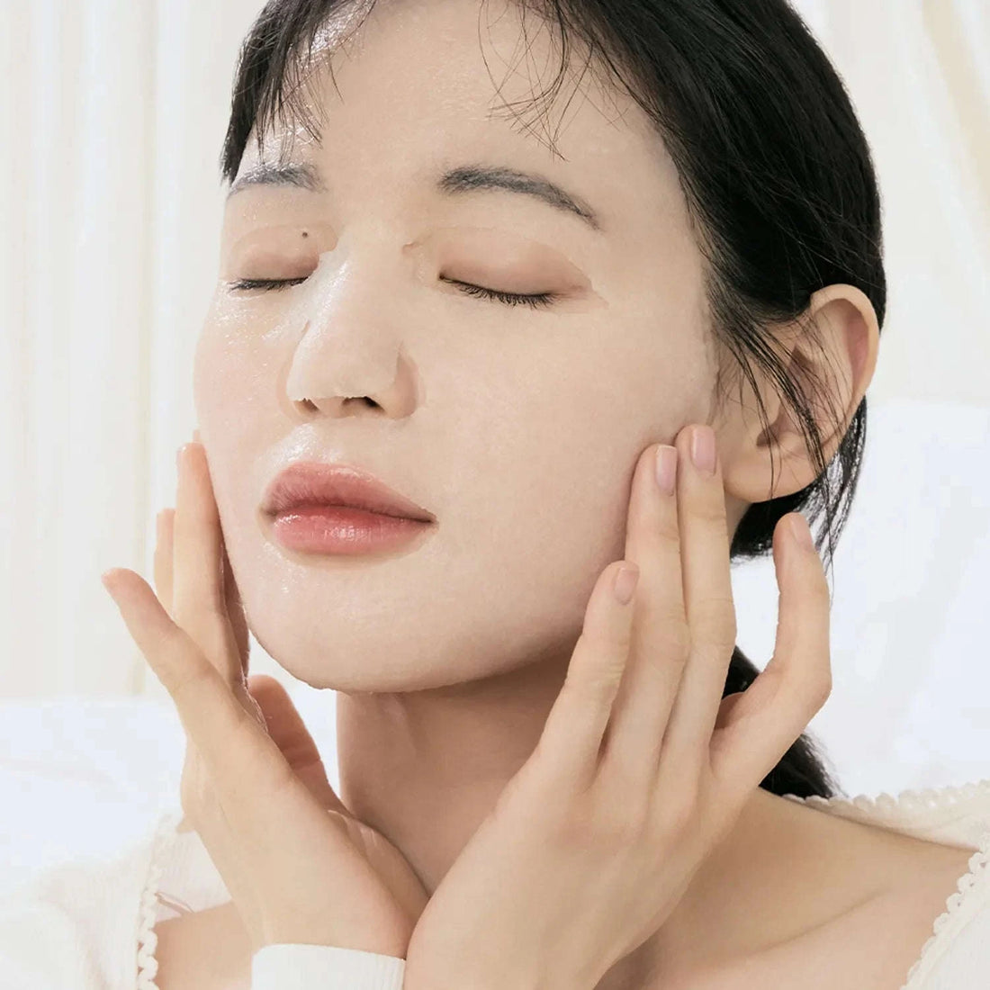 Uma mão segura a máscara facial Jelly Seal Dewy Mask da Dr. Althea em folha translúcida por cima da respetiva embalagem. A embalagem apresenta a marca e benefícios como hidratação e equilíbrio para pele sensível. O ambiente transmite calma e foco em cuidados de pele.