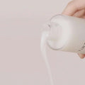 Close-up de mão despejando loção coreana branca cremosa de frasco de cosmético.