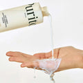 Uma mão verte o tónico Oat PDRN Gentle Refining Toner líquido de textura leitosa de um frasco para a palma da mão. A imagem transmite uma sensação de frescura e limpeza, com uma estética minimalista.