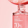 Sérum facial coreano Anua Peach 70 Niacinamide em frasco transparente com líquido rosa, detalhes de pêssego e bolhas.