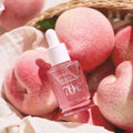 Sérum facial coreano Anua Peach 70 Niacin com embalagem conta-gotas entre pêssegos frescos