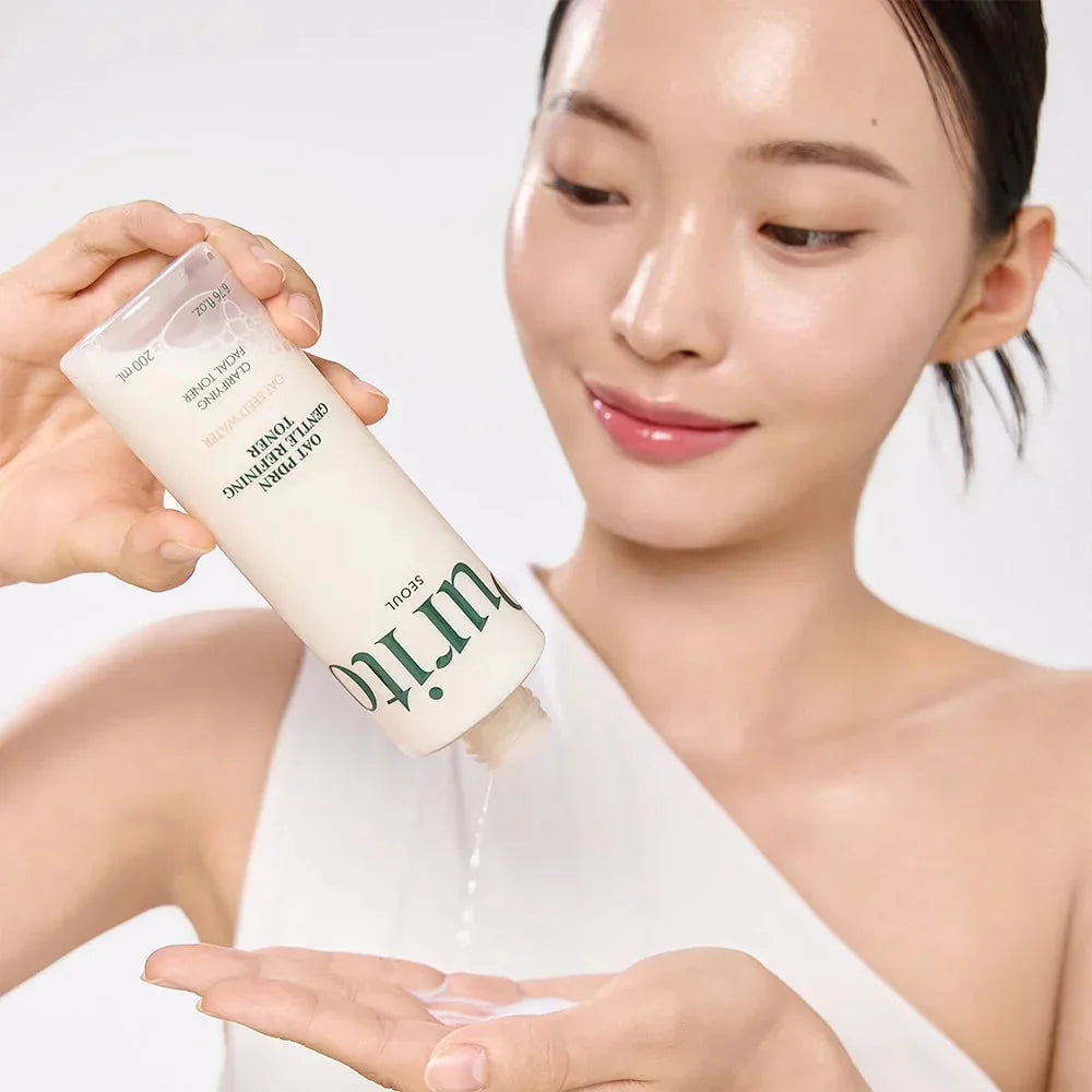 Uma mulher com pele luminosa sorri enquanto verte o tónico Oat PDRN Gentle Refining Toner de um frasco para a mão. A imagem transmite uma sensação de frescura e de ritual de cuidados de pele.