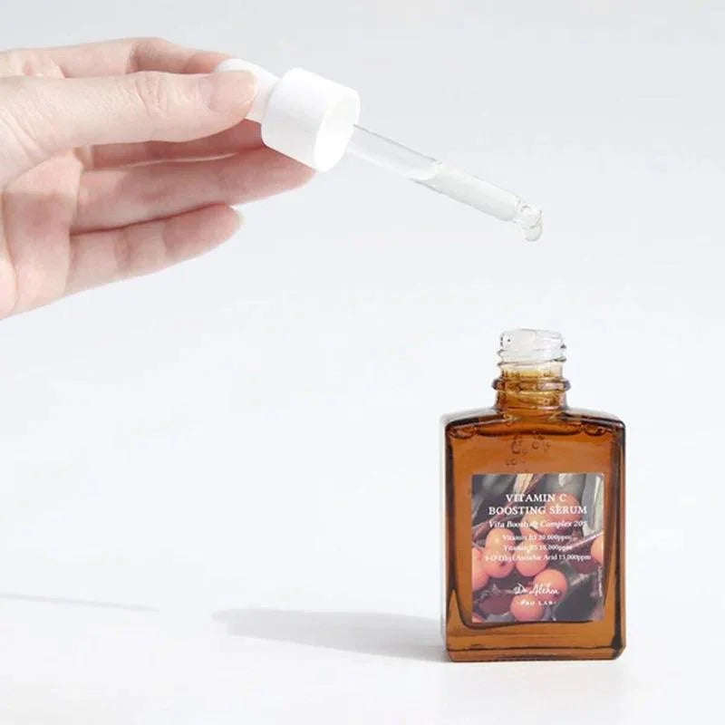 Soro facial coreano com vitamina C em frasco âmbar, conta-gotas transparente sendo usado.